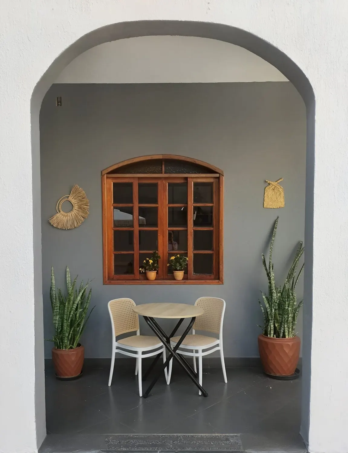 Entrada em arco da varanda da Casa Violeta, com mesa, cadeiras e plantas